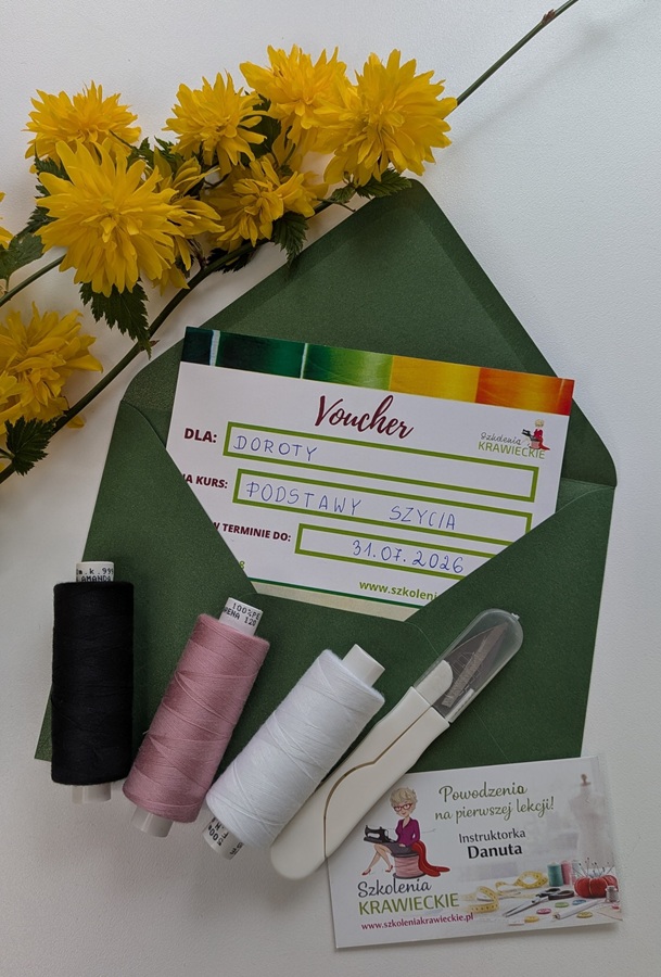 Voucher prezentowy na kurs szycia Danuty Zaczek umieszczony w ozdobnej kopercie wśród nici, przyborów krawieckich i żółtych kwiatów. Voucher można wykorzystać na kursy szycia stacjonarne w Rumi oraz kursy online dostępne dla uczestników z całej Polski.